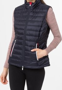 Marineblå vadderad väst med hög krage, framzipper och två sidofickor, med kontrasterande vita dragkedjor och röda detaljer. Slät textur.