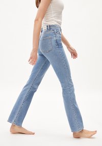 Vaaleansiniset farkut, joissa on leveä lahje, korkeaa vyötäröä, viisi taskua ja ompeluyksityiskohtia. Silkkinen rakenne, hieman kulunut ilme.