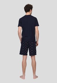 T-shirt bleu marine à manches courtes associé à un short bleu marine à motifs comportant de petits designs rouges et blancs, vu de dos.