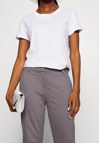 Vit bomulls-t-shirt med uppvikta ärmar, parat med grå, något åtsittande byxor. Håller en liten metallic silverväska.