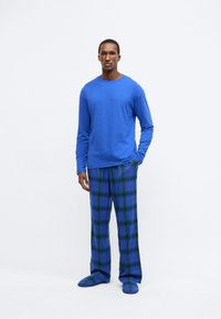 Modrá košeľa s dlhým rukávom a zelené, modré a červené kárované pyžamové nohavice s rovnakými papučami. Hladká látka, voľný strih a pohodlný dizajn.