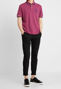 Kastanjefärgad polo med krage, logodetalj, korta ärmar med blå accenter. Matchas med slim-fit svarta byxor och svarta sneakers.