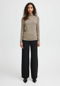 Top de tortuga de manga larga en color caqui combinado con pantalones de pierna ancha negros de talle alto. La parte superior tiene una textura suave; los pantalones son de una tela con un ajuste estructurado.