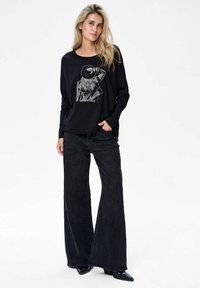 Zwarte lange mouw top met een grafische illustratie. Gecombineerd met brede zwarte jeans en zwarte hakken. Soepele stofstructuur.