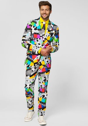 Colorful suit featuring geometric patterns in black, white, pink, green, yellow, and blue; paired with a bright yellow shirt and white sneakers.
