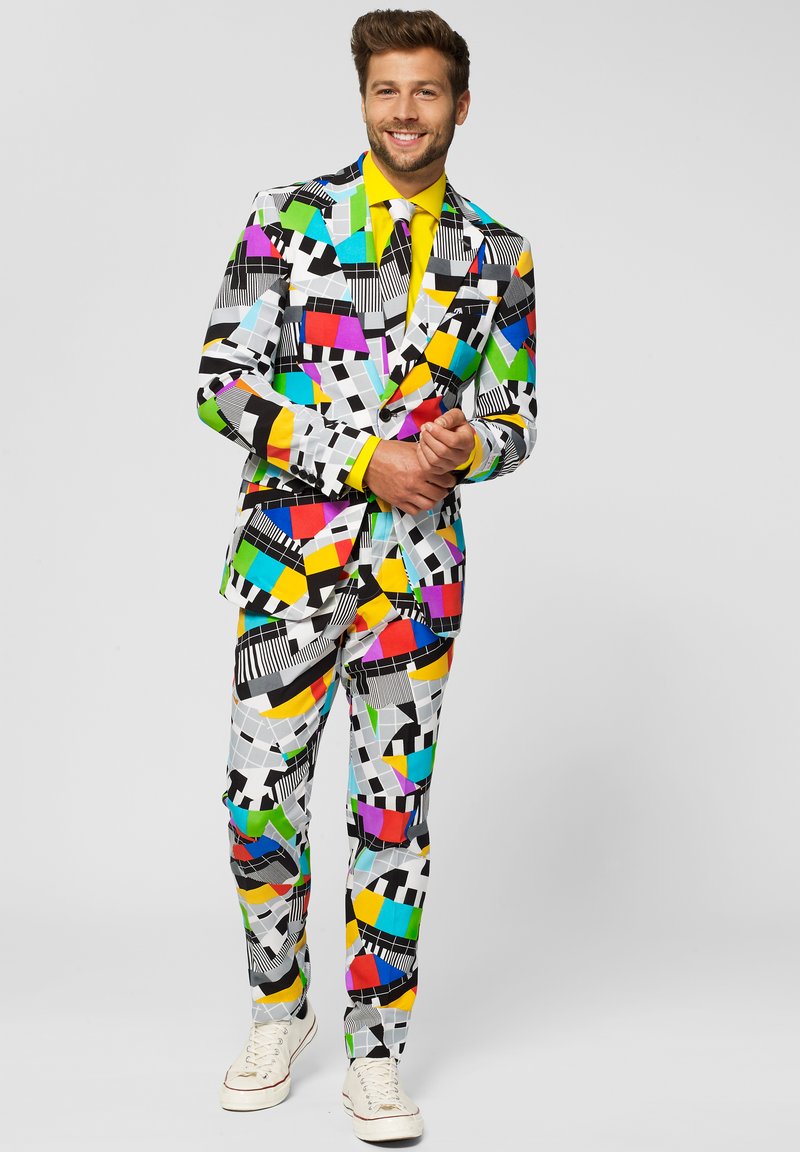 Colorful suit featuring geometric patterns in black, white, pink, green, yellow, and blue; paired with a bright yellow shirt and white sneakers.