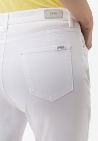 Vita denim-jeans med en medelhög passform och ett karakteristiskt bakfickdesign. Har en läderlapp med varumärket "BRAX" och subtila dekorativa detaljer.