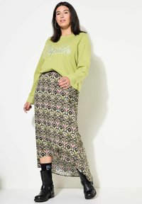 Groene sweater met de tekst "Capable", bloemenpatroon maxi rok in groen, roze en zwart, gecombineerd met zwarte enkellaarsjes.