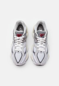 Para białych i szarych sneakersów New Balance 9060 z siateczkowymi i zamszowymi panelami, białymi sznurówkami oraz czerwonym detalem logo na języku, widziane z góry.