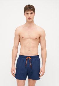 Námořnické plavky s elastickým pasem a jasně oranžovým šňůrkou na stažení. Lehce materiál, délka nad kolena, minimální branding.