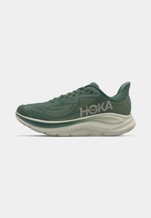Grønne sportsko med mesh-overdel, polstret krave, tyk hvid mellemsål og gummiydersål; har "HOKA" logo på siden.