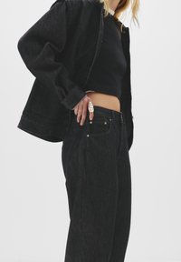 Zwarte denim jack en hoge taille spijkerbroek, met een klassiek snit, contrasterende stiksels en metalen knoopdetails. Glad, textuurrijke stof.