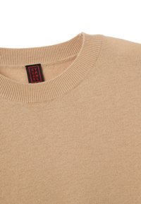 Maglione beige con colletto a girocollo a coste. Realizzato in materiale morbido, presenta un'etichetta con colori rosso e nero. Texture liscia senza motivi visibili.