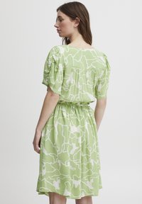 Rochie verde cu modele abstracte albe, mâneci scurte tip puff, talie elastică și fustă fluida. Material moale cu o croială lejeră.