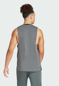 Maillot de sport sans manches gris avec un col rond et des fentes sur les côtés. Fabriqué en tissu léger, il présente une texture lisse et un branding minimal.