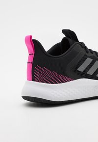 Černá sportovní bota s texturovaným síťovaným svrchem, šedými akcenty a růžovým poutkem. Bílá střední podrážka s černou vzorovanou podrážkou.