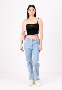 Fekete bársonyból készült, spagetti pántos cropped top, világoskék egyenes lábú farmer és egy kis rózsaszín táska; a modell egy fehér háttér előtt áll.
