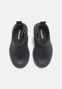 Černé kožené kotníkové boty se bočními zipy, hladký povrch, kulatá špička a kontrastní vnitřní podšívka. Logo Timberland viditelné uvnitř.