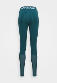 Teal Nike leggings met meshpanelen op de kuiten en een brede tailleband met herhaaldelijk wit Nike-logo op een effen achtergrond.