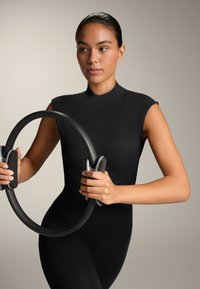 Črn oprijet outfit z visoko vratnim izrezom in kratkimi rokavi; drži črni odporni obroč s sivo gumo za prijem. Gladke teksture, minimalistična zasnova.