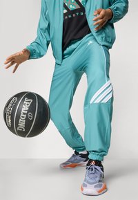turkis joggedrakt med hvite detaljer, teksturert sporty stoff, elastiske mansjetter; grå og oransje sneakers; svart basketball med hvit logo.