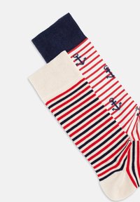 Rot-weiß gestreifte Socken mit navyblauen Akzenten. Eine Socke hat Anker-Muster, während die andere ein einheitliches cremefarbenes Design hat. Aus weichem Baumwollmaterial.