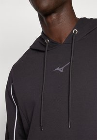 Black hoodie with drawstrings and metal eyelets, featuring a subtle logo in gray. The fabric appears smooth with white accent lines on the sides.