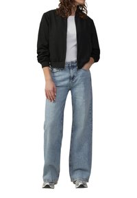 Zwarte bomberjack met ribgebreide manchetten, gecombineerd met lichtblauwe wijde jeans. Sneakers hebben een zilveren accent. Eenvoudig ontwerp, casual pasvorm.