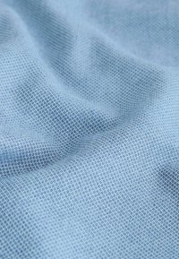 Tissu bleu clair texturé avec un petit motif répétitif en losanges et de doux plis créant des ombres délicates.