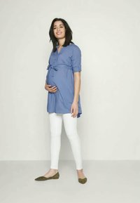 Tunic blu da maternità con maniche corte, fiocco in vita, abbinata a leggings bianchi e ballerine verdi. Tessuto morbido, vestibilità rilassata.