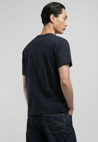 T-shirt in cotone blu navy con maniche corte e vestibilità rilassata, vista da dietro, abbinato a jeans in denim scuro con cuciture a contrasto.