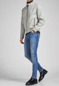 Grijze nep leren jas met een staande kraag, rits aan de voorkant en zijzakken. Gedragen over een zwart shirt en gecombineerd met blauwe slim-fit jeans en zwarte laarzen.