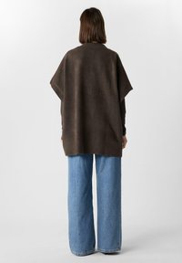 Brązowy dzianinowy ponczo o luźnym kroju, z krótkimi rękawami i ribbowymi brzegami, w połączeniu z jasnoniebieskimi spodniami typu wide-leg.