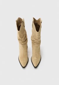 Bottes en suède tan jusqu'aux genoux avec un design décontracté, bout pointu et semelle en caoutchouc noir. Pas de matériel ou de motifs visibles.
