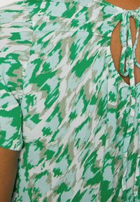 Grøn- og hvidmønstret bluse med struktureret finish, med en udskåret ryg og båndlås. Korte ærmer og afslappet pasform.
