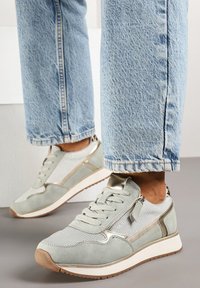 Baskets vert clair avec tige en mesh, accents en daim, finition métallique et fermeture éclair sur le côté. Semelle blanche avec un profil de bandeau texturé en brun.