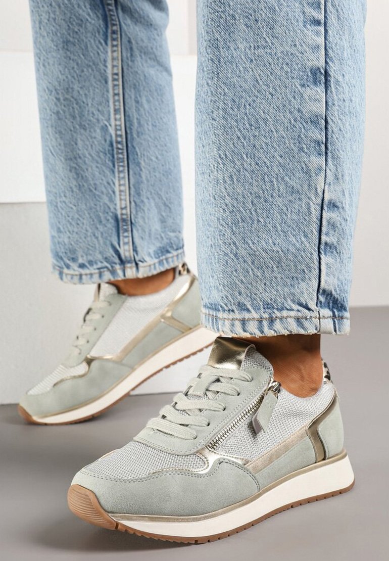 Baskets vert clair avec tige en mesh, accents en daim, finition métallique et fermeture éclair sur le côté. Semelle blanche avec un profil de bandeau texturé en brun.