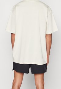 Kortärmad, krämfärgad T-shirt med avslappnad passform och rak nederkant. Mjukt bomullsmaterial, minimalistisk design, utan synliga mönster eller accenter.