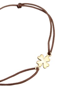 Bracelet en corde tressée marron avec un charm en or en forme de trèfle à quatre feuilles, aux bords lisses et à la finition polie. Taille ajustable pour le port.
