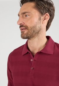 Bordeaux polo shirt met een gestructureerd ontwerp, drie-knopen placket en een klassieke kraag. Zachte stof met een horizontaal streepje patroon.