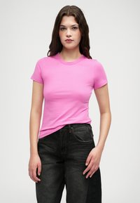 Dopasowana różowa bawełniana koszulka z krótkim rękawem i okrągłym dekoltem, zestawiona z ciemnoniebieskimi dżinsami o wysokim stanie. Prosty design, bez wzorów ani grafik.