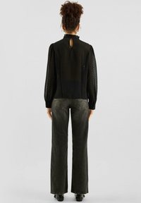 Zwarte blouse met getextureerde stippen, hoge halslijn en keyhole-rug. Gecombineerd met grijze jeans met wijde pijpen en zwarte enkellaarzen.