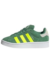 Zapatillas de ante verde con tres llamativas rayas amarillas, suela de goma blanca, detalles perforados y un acento gris en el talón.