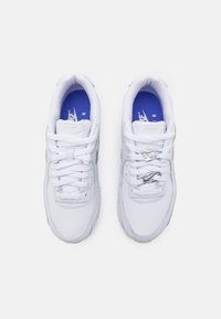 Paire de baskets blanches Nike Air avec semelles intérieures bleues, vues de dessus, avec des lacets classiques à gauche et des lacets sans nouer à droite.