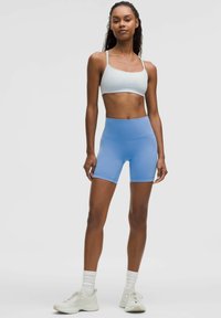 Svijetloplave atletske kratke hlače s visokim pojasom, glatkom teksturom i prilagođenim dizajnom. Uparene s bijelim sportskim grudnjakom i svijetlim tenisicama.