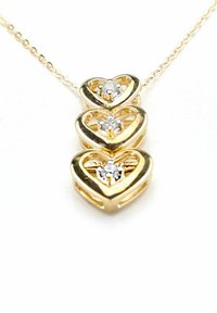 Collana a forma di cuore in oro con tre cuori sovrapposti, ciascuno caratterizzato da una piccola gemma trasparente al centro. Texture liscia e finitura lucida.