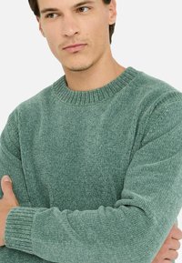 Maglione a coste verde aderente con scollatura rotonda a coste e tessuto testurizzato, dotato di maniche lunghe e polsini a coste.