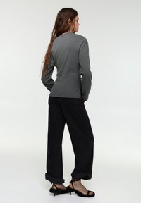 Siv dolg rokav top, oprijet v pasu, kombiniran z ohlapnimi črnimi hlačami z zavihanimi hlačnicami. Črne sandale s peto s krznenimi poudarki.