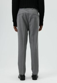 Grijze op maat gemaakte broek met een gladde textuur, voorzien van twee achterzakken en een rechte pijp. Draagt bijpassend een zwarte geribbelde trui.