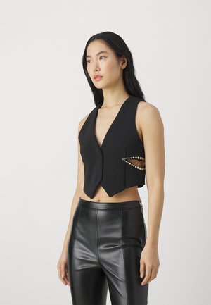 Svart cropped vest laget av glatt stoff med dyp V-hals, knapp-forside og utsmykkede sideutskjæringer med metalliske detaljer.